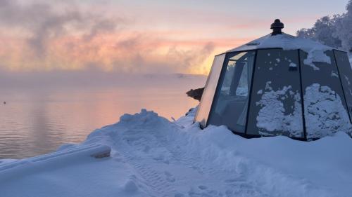 a tent covered in snow next to a body of water at Aurora Sea Lodges AURORAHUT in Herjenes