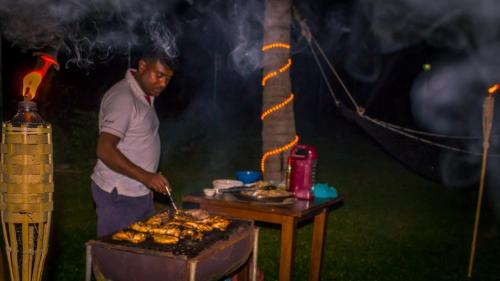a man is cooking food on a grill at Serenity Lake Resort Yala in Tissamaharama