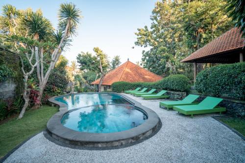 a swimming pool with green lounge chairs and trees at Argasoka Bungalows in Ubud