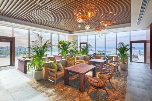 a lobby with tables and chairs and windows at HOTEL AlaCOOJU OKINAWA in Urazoe