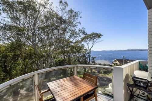 a deck with a wooden table and chairs on a balcony at Tranquil Escape - Koala Hotspot - 2 Bed 2 Bath Apt Spectacular Sea Views in Soldiers Point