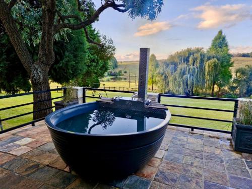 a large black tub sitting on a patio with a tree at Luxury Country Retreat Hot Tub & Farm Views in Dullstroom