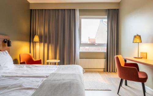 a hotel room with a bed and a desk and chairs at ProfilHotels Grand Kristianstad in Kristianstad