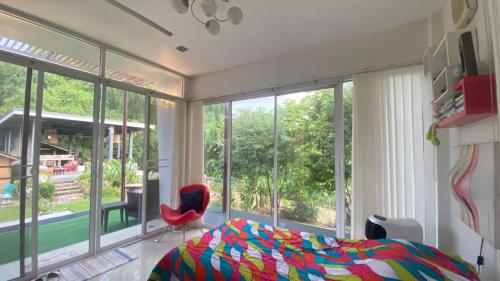 a bedroom with a bed and a red chair and windows at Mae Wad House in Ban Oi