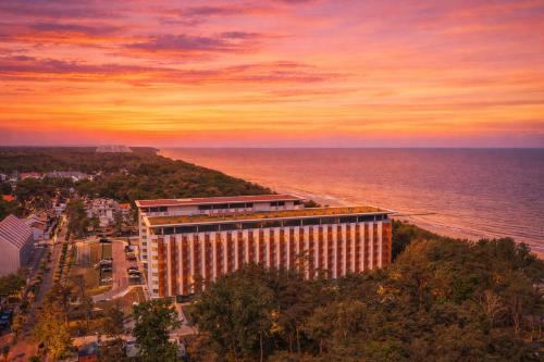 a building in front of the ocean at sunset at Prestige 204 - tuż przy plaży - Easy-Rent Apartments in Pobierowo