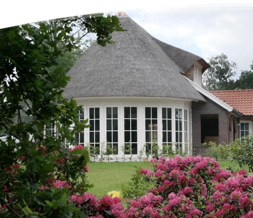 a house with a thatched roof and pink flowers at Outdoors Holten - Cabin Skydeck in Holten