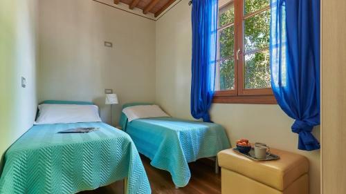 two beds in a room with blue curtains and a window at Petriolo - Tuscany Hills & Jacuzzi in Cerreto Guidi