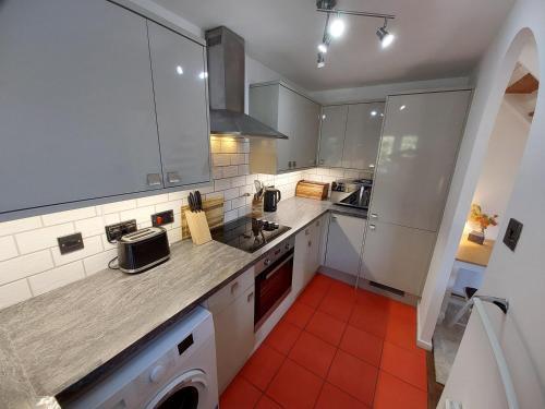 a kitchen with white cabinets and an orange tile floor at 2 beds, AC, fully enclosed patio, private parking in Poole