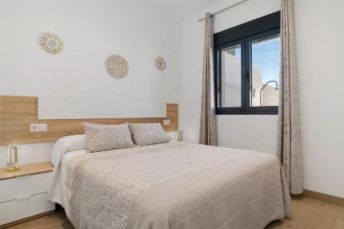 a white bedroom with a bed and a window at Casas Las Arenas 2 in Conil de la Frontera