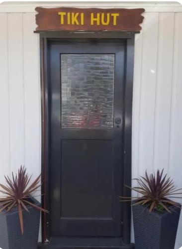 a black door with a sign above it with two plants at Tiki Hut in Tauranga
