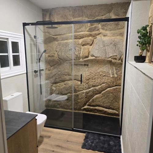 a shower in a bathroom with a stone wall at Casa a Figueira in Pungín