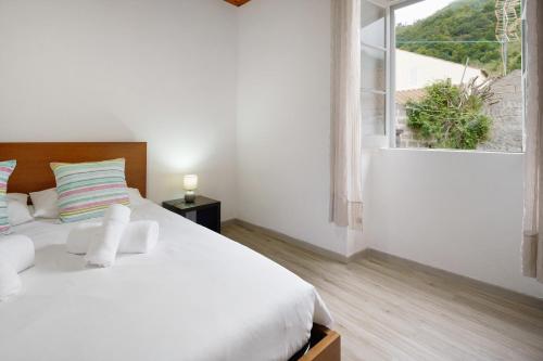 a white bedroom with a large bed and a window at Casa Flor de Laranjeira in Faial da Terra