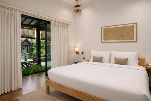 a bedroom with a large white bed and a sliding glass door at Moringa Tree Maison in Siem Reap