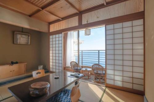 a room with a table and chairs and a large window at Hokkawa Onsen Hotel in Higashiizu