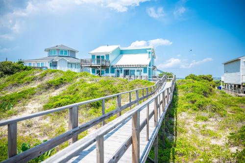 a blue house on top of a hill with a boardwalk at Beach Buzz by Oak Island Accommodations in Caswell Beach