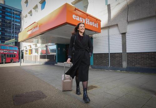 a woman standing in front of a store with a suitcase at easyHotel Croydon in Croydon