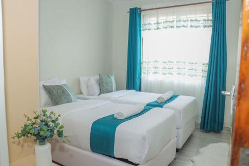 two beds in a room with blue curtains and a window at D&H Homes Milimani Nakuru-Elegant 2 Bedroom Apartment in Nakuru