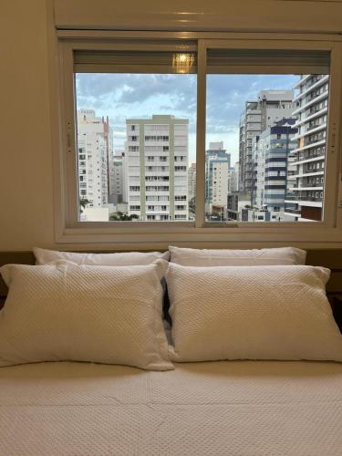 a bed with white pillows in front of a window at Apartamento Completo Duas Quadras do Mar in Capão da Canoa
