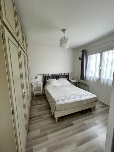 a white bedroom with a bed and a dresser at La case du trimaran in Cabourg