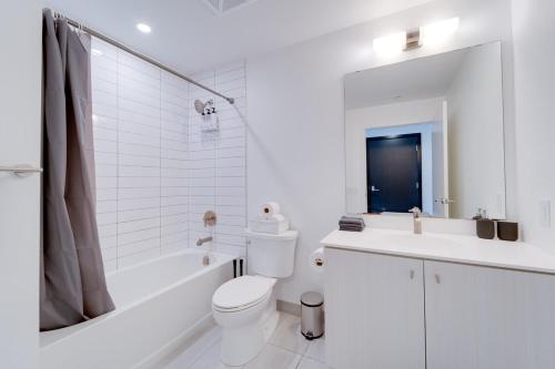 a white bathroom with a toilet and a tub and a sink at Modern Downtown Condo with Gym in Kitchener