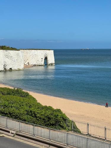 a person walking on a beach next to the ocean at Broadstairs Beach Holiday Apartments, opposite Kingsgate Bay with a parking space in Broadstairs