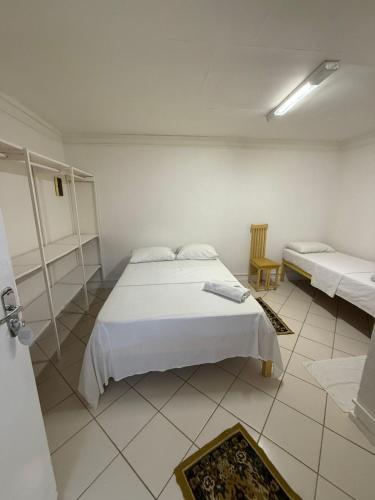 a white bedroom with two beds and a chair at Bahia Executivo Pousada in Zeca