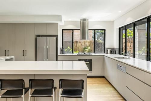a kitchen with a white counter and chairs in it at Stone & Sand in Lennox Head