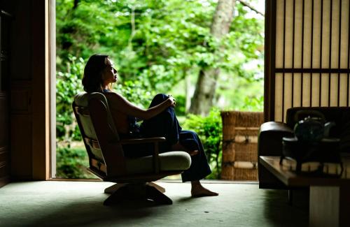 a woman sitting in a chair looking out a window at Oukai Villa Izumi in Izumi