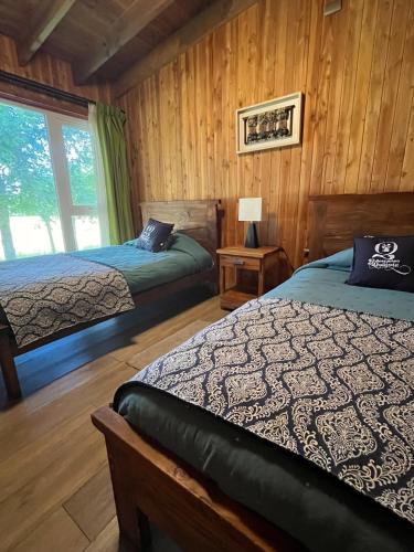two beds in a room with wooden walls at El Descanso del Quijote in Riñinahue