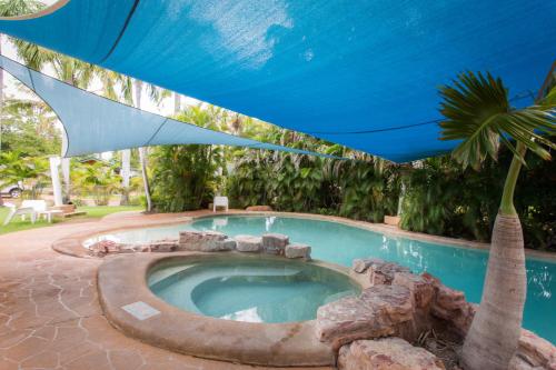 ein Pool mit einem blauen Regenschirm und einer Palme in der Unterkunft Ivanhoe Resort in Kununurra