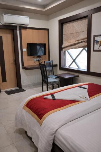 a bedroom with a bed and a chair and a television at Hotel Benaras Gharana Inn in Varanasi