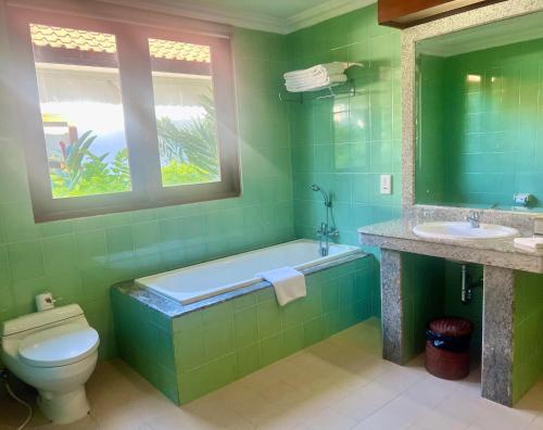 a green bathroom with a tub and a toilet and a window at Peninsula Villa in Nusa Dua