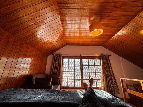 a bedroom with a wooden ceiling with a bed and a window at Mistvale Cottage in Manāli
