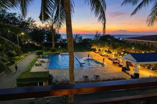 a resort with a pool and palm trees at sunset at Bason Hotel Long Hải in Long Hai