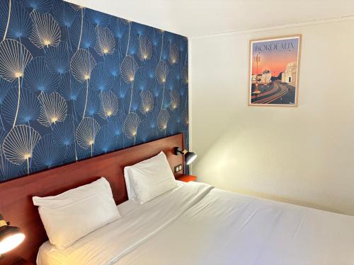 a bedroom with a bed and a blue wall at Kyriad Bordeaux Lormont in Lormont