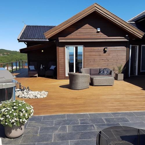 a wooden deck with a couch on a house at Luxury Fjord Cabin with jacuzzi, boat dock & view in Sveio