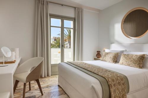 a white bedroom with a bed and a desk and a window at Tzanis Resort Skyros in Skiros