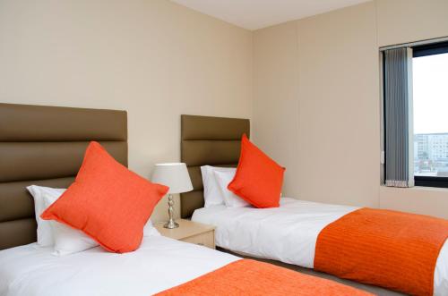 two beds with orange pillows in a room at Knightsbridge Luxury Apartments in Cape Town