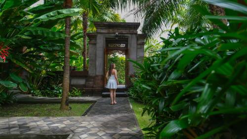 a woman in a white dress walking through a garden at Griya Shanti Suites in Sanur