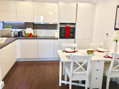 a kitchen with white cabinets and a white table and chairs at 2-Bedrooms Modern Apartment next to Velodrome, Lounge, Balcony, Parking, ABBA in London