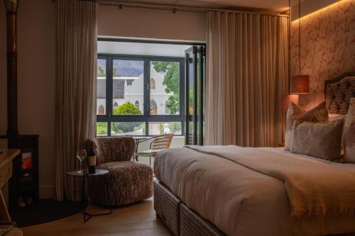 a bedroom with a bed and a chair and a window at Le Petit Manoir Boutique Hotel in Franschhoek
