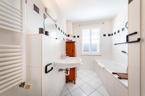 a white bathroom with a sink and a tub at Haus Arrewind in Ahrenshoop