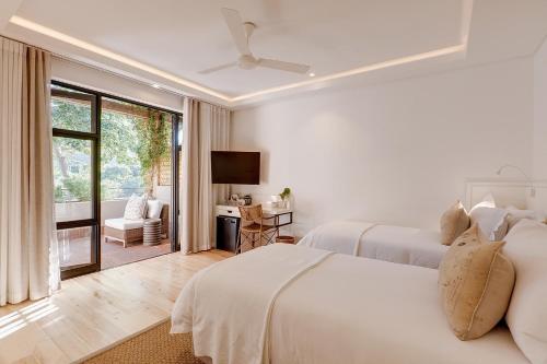 a white bedroom with two beds and a television at Barrington's in Plettenberg Bay