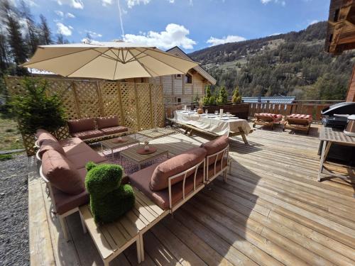 a wooden deck with a couch and an umbrella at Chalet La Tanière 14 Pers - piscine chauffée et sauna - Vars Saint Marcellin in Vars