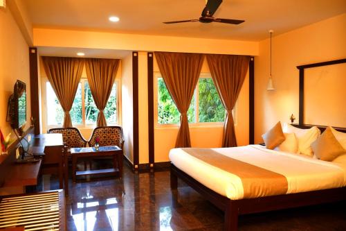 a bedroom with a bed and a desk and windows at DNC Shevaroys Resorts & Spa in Yercaud