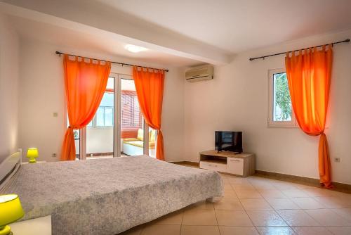 a bedroom with orange curtains and a bed and a television at Mango Apartment Petrovac in Petrovac na Moru