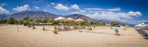 a sandy beach with umbrellas and chairs and mountains at Poseidon Studios in Georgioupolis