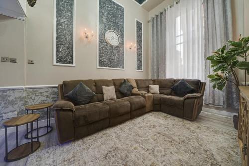 a living room with a brown couch and a clock on the wall at Luxurious Royal 2BR Apartment, Glasgow City Centre in Glasgow