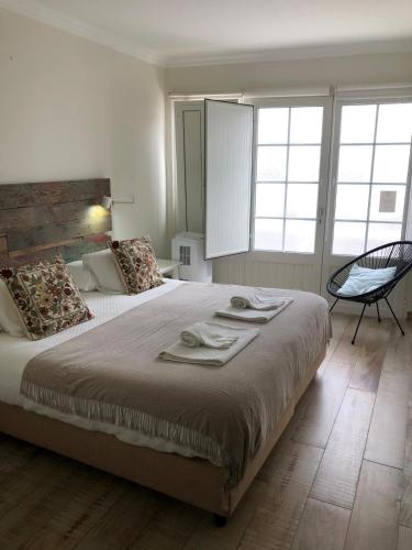 a bedroom with a large bed and a chair at Pé na Areia, Alojamento Local in Porto Covo