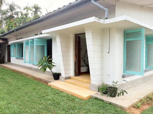 a white house with blue shutters and a porch at Achcha's Place in Negombo